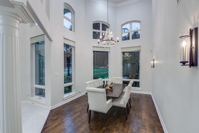 dining space featuring a high ceiling, a healthy amount of sunlight, wood finished floors, a chandelier, and baseboards