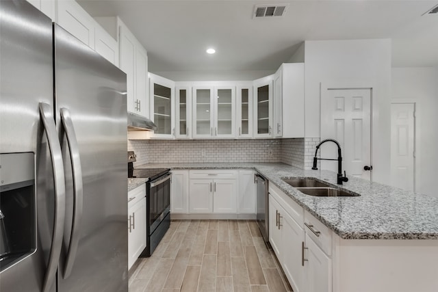 kitchen with light stone countertops, sink, backsplash, white cabinets, and appliances with stainless steel finishes