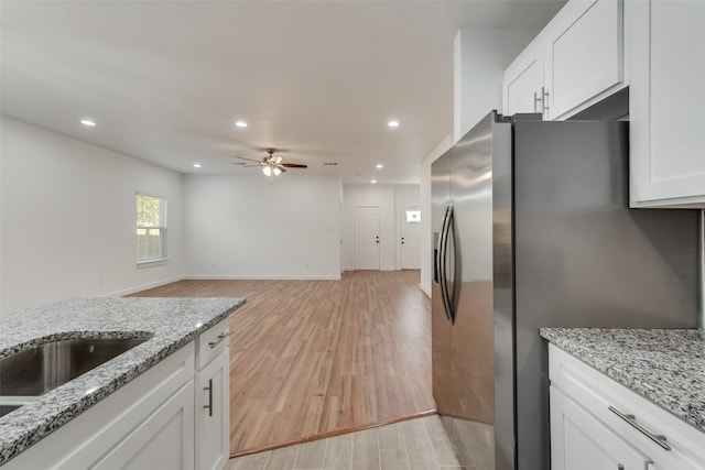 kitchen with stainless steel fridge, light stone counters, white cabinetry, and light wood-type flooring