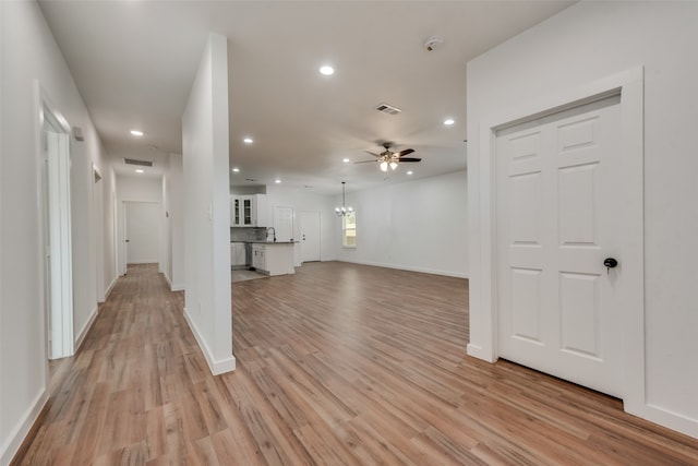 unfurnished living room featuring ceiling fan with notable chandelier and light hardwood / wood-style floors