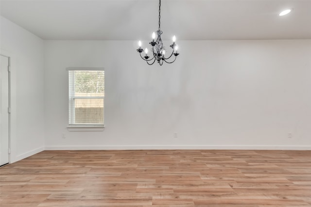 spare room with a chandelier and light wood-type flooring