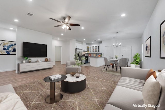 living room with ceiling fan with notable chandelier and wood-type flooring