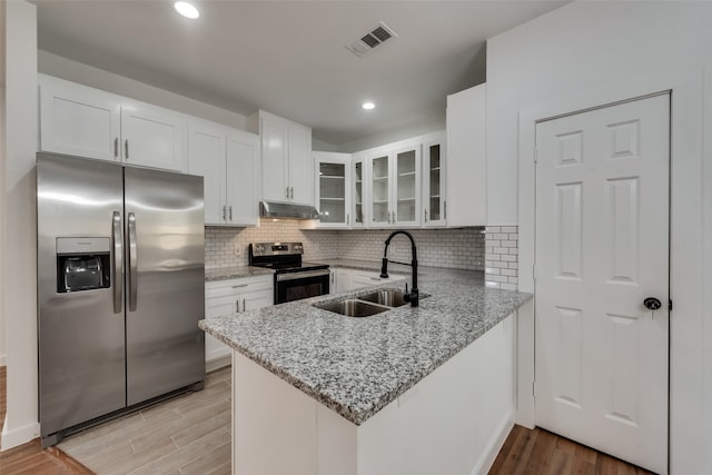 kitchen with kitchen peninsula, light stone countertops, white cabinetry, and stainless steel appliances