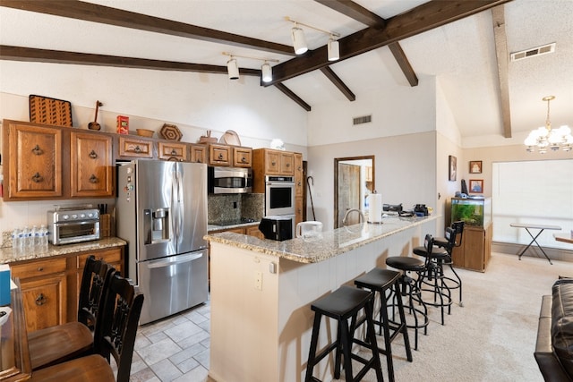 kitchen with a chandelier, light colored carpet, beam ceiling, light stone countertops, and appliances with stainless steel finishes