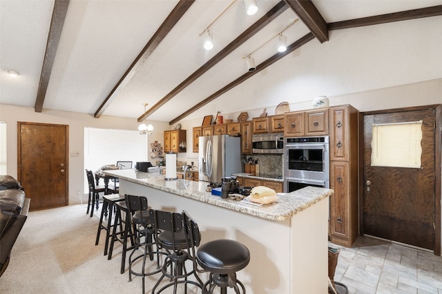 kitchen featuring stainless steel appliances, a kitchen island, light stone countertops, a breakfast bar, and beamed ceiling