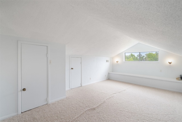 additional living space with a textured ceiling, light carpet, and vaulted ceiling