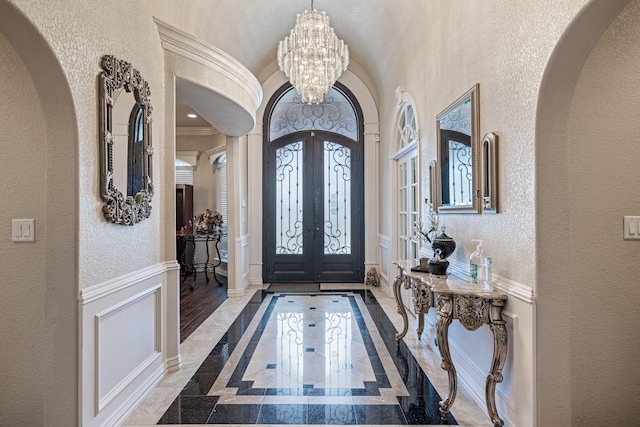 foyer entrance with a notable chandelier, french doors, hardwood / wood-style floors, a healthy amount of sunlight, and ornamental molding