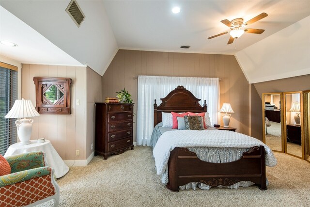 bedroom with wood walls, vaulted ceiling, light colored carpet, and ceiling fan