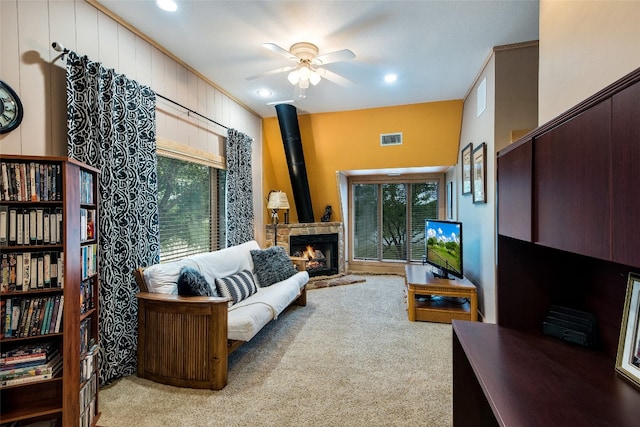 carpeted living room with a stone fireplace and ceiling fan