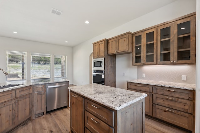 kitchen featuring a kitchen island, stainless steel appliances, sink, light stone countertops, and light wood-type flooring