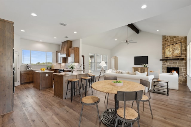 dining area with a stone fireplace, vaulted ceiling with beams, light wood-type flooring, and ceiling fan