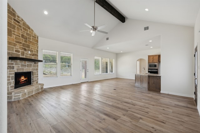 unfurnished living room with a stone fireplace, light hardwood / wood-style floors, ceiling fan, beamed ceiling, and high vaulted ceiling