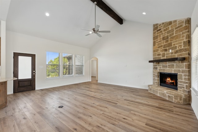 unfurnished living room with a stone fireplace, ceiling fan, beamed ceiling, high vaulted ceiling, and light hardwood / wood-style flooring