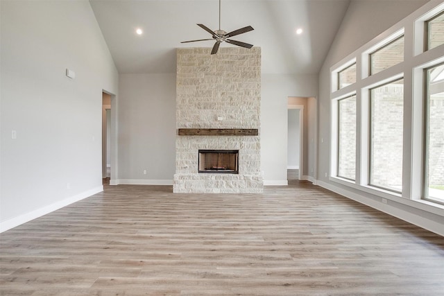 unfurnished living room featuring high vaulted ceiling, a stone fireplace, ceiling fan, and light hardwood / wood-style floors