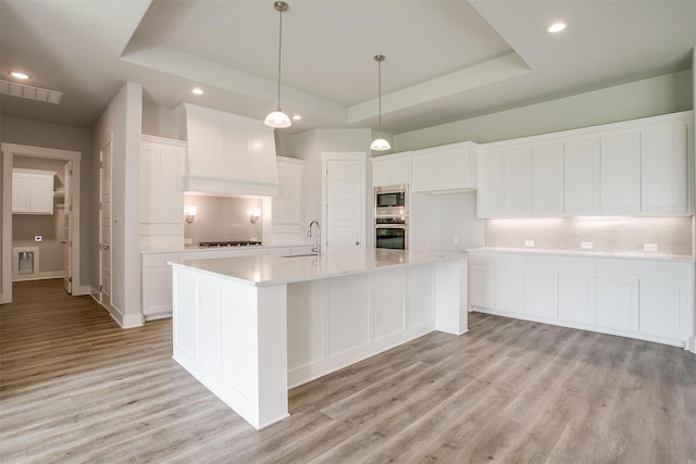 kitchen with appliances with stainless steel finishes, a raised ceiling, sink, a center island with sink, and white cabinetry