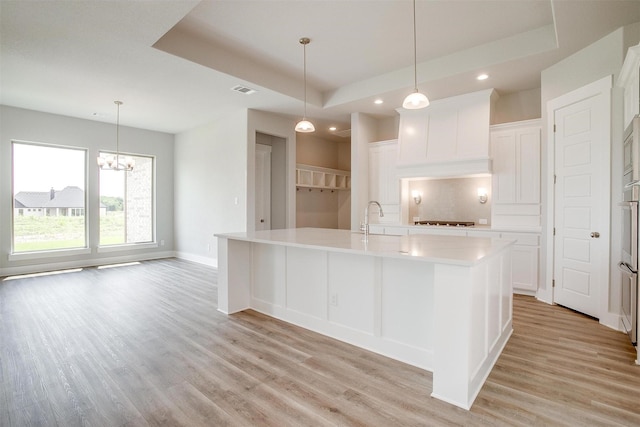 kitchen with white cabinets, a raised ceiling, a spacious island, and sink