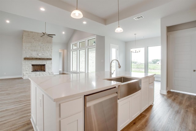 kitchen with white cabinetry, sink, hanging light fixtures, stainless steel dishwasher, and a kitchen island with sink