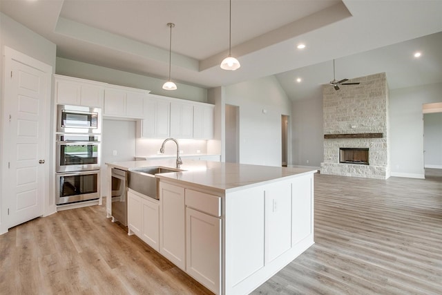 kitchen featuring sink, an island with sink, a tray ceiling, a fireplace, and white cabinets