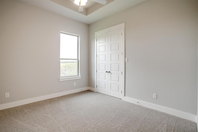 unfurnished bedroom featuring carpet, a closet, ceiling fan, and a tray ceiling