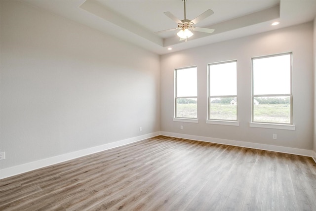 empty room with ceiling fan, a raised ceiling, and light hardwood / wood-style flooring