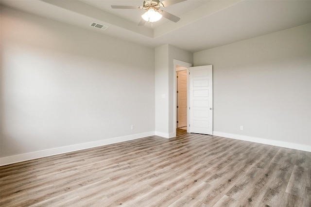 unfurnished room featuring a raised ceiling, ceiling fan, and light wood-type flooring