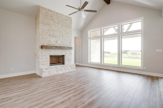 unfurnished living room featuring ceiling fan, beam ceiling, high vaulted ceiling, light hardwood / wood-style flooring, and a stone fireplace