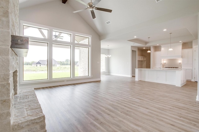 unfurnished living room with ceiling fan with notable chandelier, a fireplace, high vaulted ceiling, and light hardwood / wood-style flooring