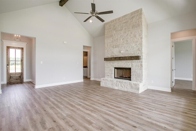 unfurnished living room with a stone fireplace, light hardwood / wood-style flooring, beamed ceiling, high vaulted ceiling, and ceiling fan with notable chandelier