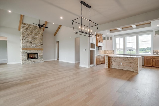 kitchen featuring beam ceiling, a brick fireplace, tasteful backsplash, white cabinets, and ceiling fan with notable chandelier