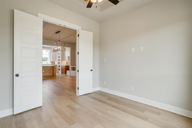 empty room with ceiling fan with notable chandelier and light hardwood / wood-style floors