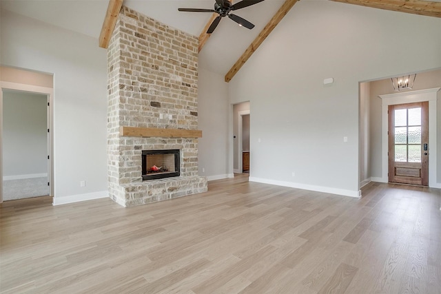 unfurnished living room featuring beam ceiling, ceiling fan, a large fireplace, light hardwood / wood-style flooring, and high vaulted ceiling