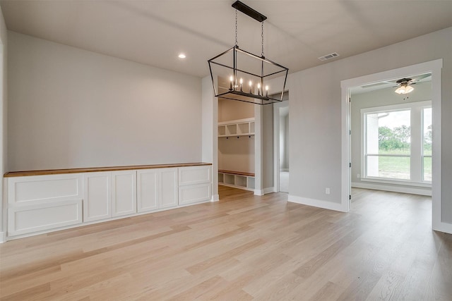 unfurnished dining area with ceiling fan with notable chandelier and light wood-type flooring