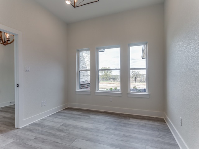 unfurnished room with a notable chandelier and light wood-type flooring