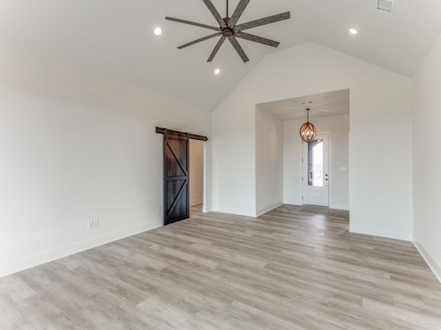 empty room featuring a barn door, lofted ceiling, ceiling fan with notable chandelier, and light wood-type flooring