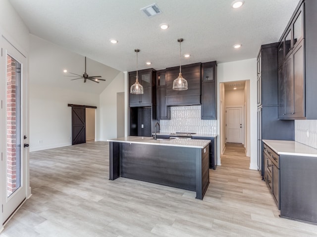 kitchen with ceiling fan, light hardwood / wood-style floors, an island with sink, vaulted ceiling, and tasteful backsplash