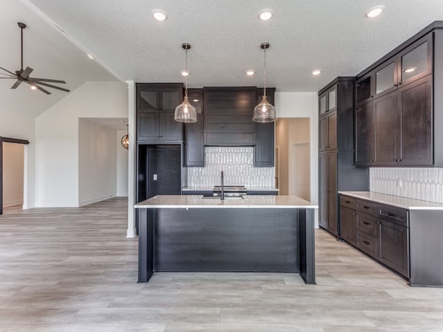 kitchen featuring light hardwood / wood-style floors, tasteful backsplash, a kitchen island with sink, pendant lighting, and ceiling fan