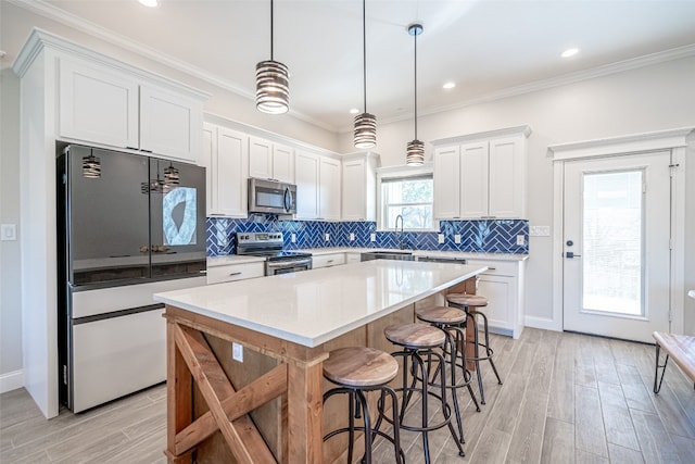 kitchen featuring a center island, hanging light fixtures, crown molding, white cabinets, and appliances with stainless steel finishes