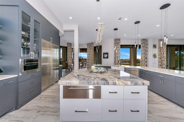 kitchen with stainless steel appliances, decorative light fixtures, a center island, light stone countertops, and gray cabinets