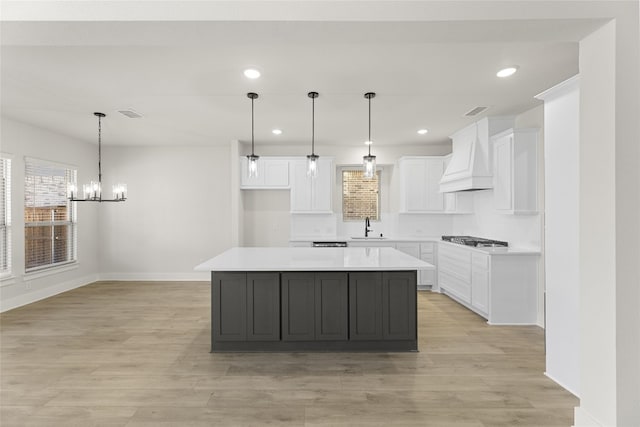 kitchen with a kitchen island, custom range hood, pendant lighting, and white cabinetry