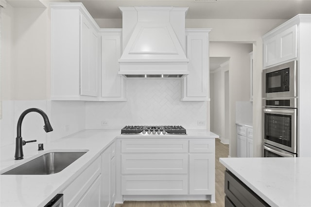 kitchen featuring appliances with stainless steel finishes, light hardwood / wood-style flooring, premium range hood, tasteful backsplash, and white cabinetry