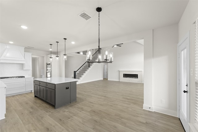 kitchen with a center island, decorative light fixtures, white cabinets, and light hardwood / wood-style flooring