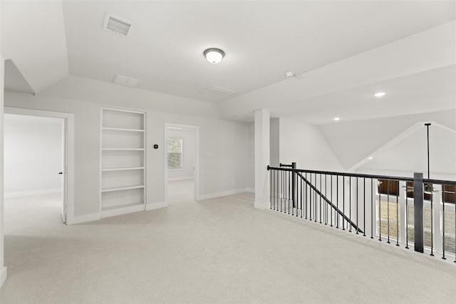 basement with built in shelves, light colored carpet, and plenty of natural light