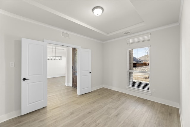 unfurnished room featuring a raised ceiling, crown molding, a notable chandelier, and light hardwood / wood-style flooring