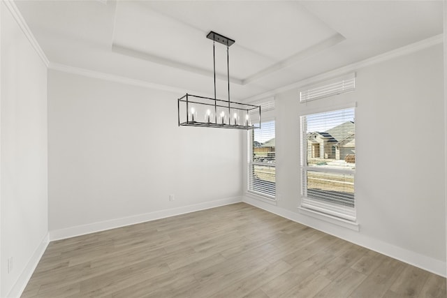 unfurnished dining area with crown molding, a notable chandelier, a tray ceiling, and light wood-type flooring