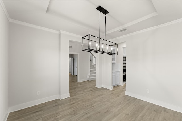 empty room with a raised ceiling, light hardwood / wood-style floors, and a notable chandelier