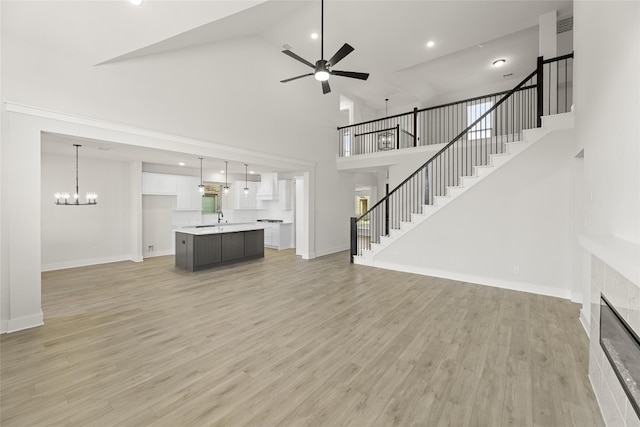 unfurnished living room with light hardwood / wood-style floors, high vaulted ceiling, ceiling fan with notable chandelier, and a tiled fireplace