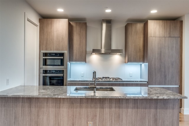 kitchen featuring appliances with stainless steel finishes, light wood-type flooring, sink, light stone countertops, and wall chimney exhaust hood