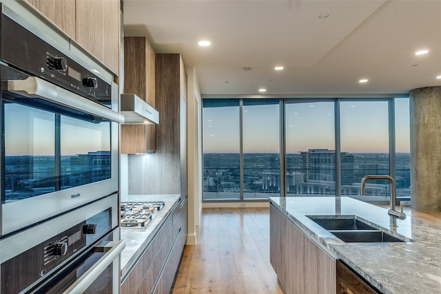 kitchen featuring light stone countertops, light hardwood / wood-style flooring, appliances with stainless steel finishes, a wall of windows, and sink