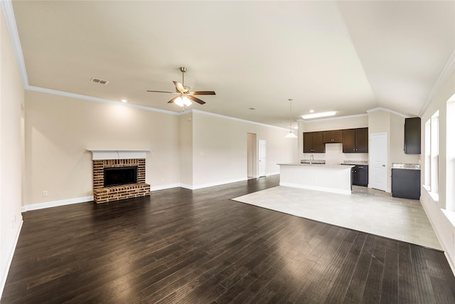 unfurnished living room with a brick fireplace, vaulted ceiling, ceiling fan, dark wood-type flooring, and crown molding