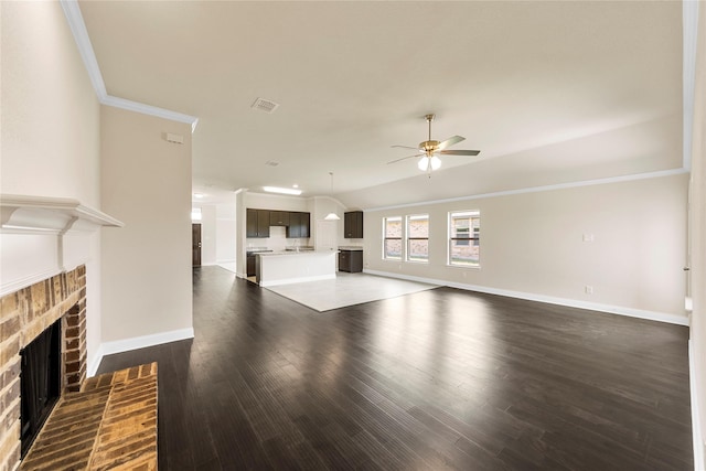 unfurnished living room featuring ceiling fan, a brick fireplace, dark hardwood / wood-style flooring, crown molding, and lofted ceiling